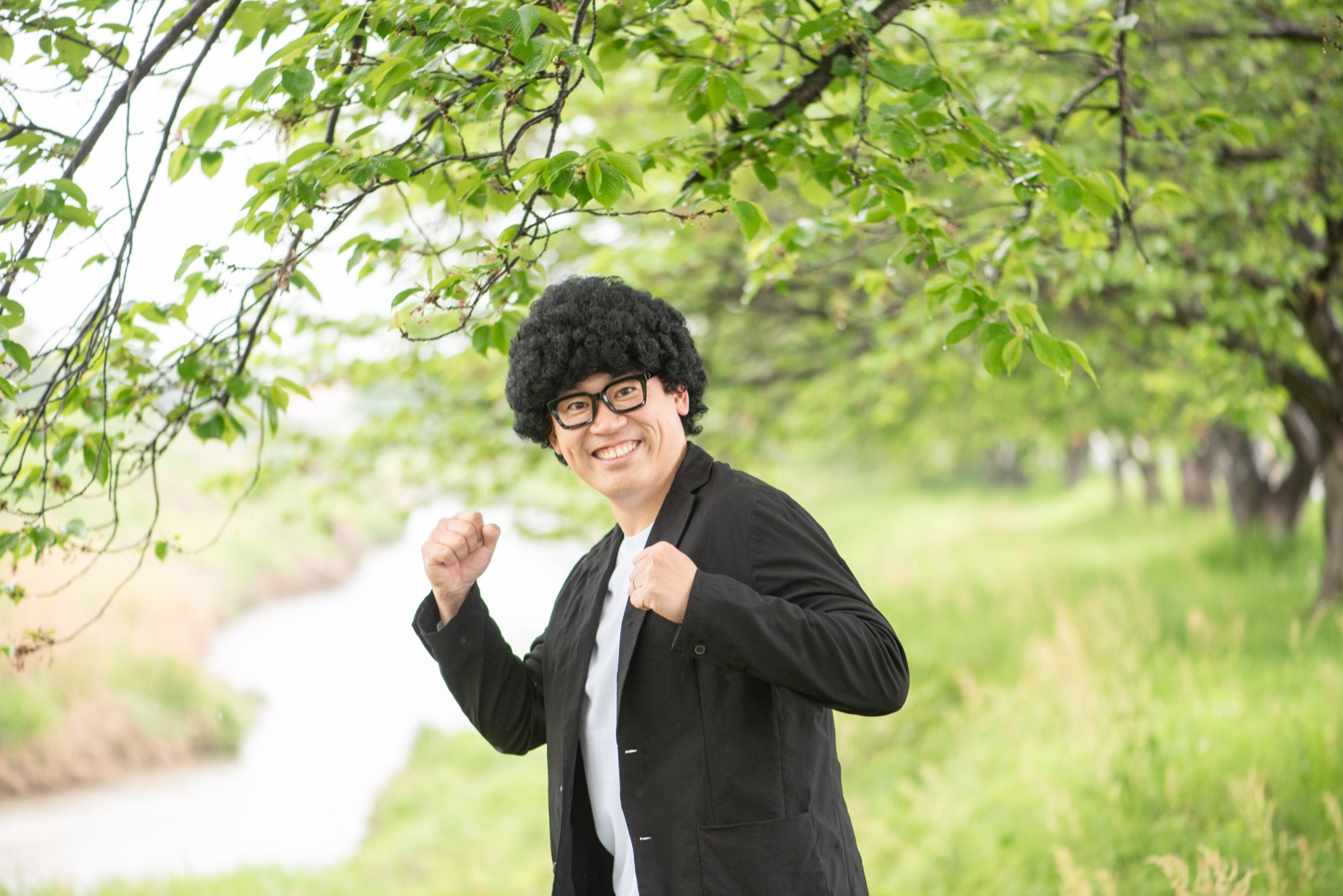 緑の木々の中で笑顔で両手を広げるキャリー先生